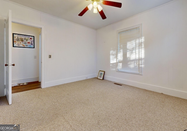 empty room featuring ceiling fan, carpet, ornamental molding, visible vents, and baseboards