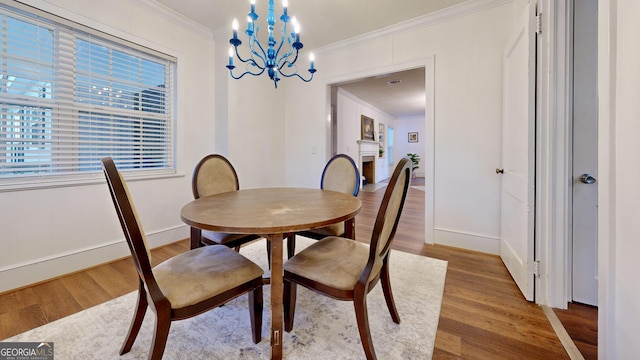 dining room featuring baseboards, a chandelier, ornamental molding, a fireplace, and wood finished floors