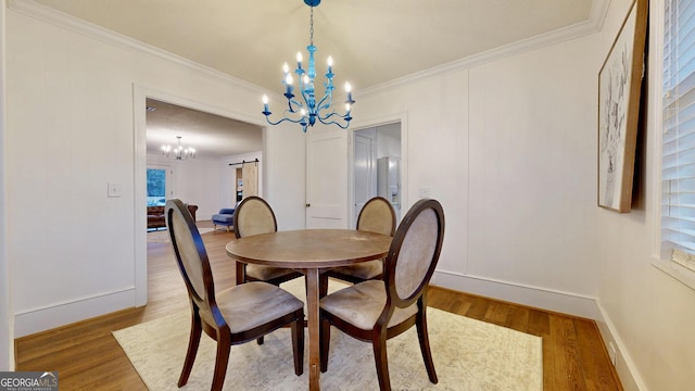 dining room with ornamental molding, wood finished floors, a barn door, an inviting chandelier, and baseboards