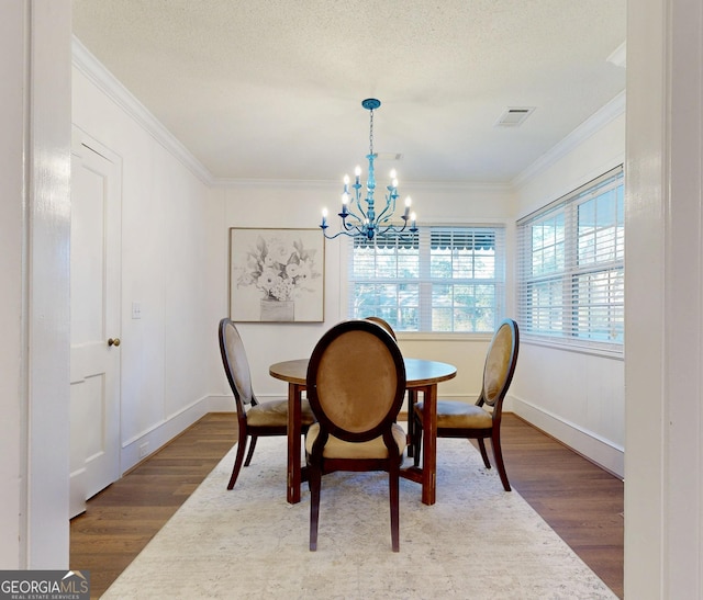 dining room featuring visible vents, a chandelier, a textured ceiling, crown molding, and wood finished floors