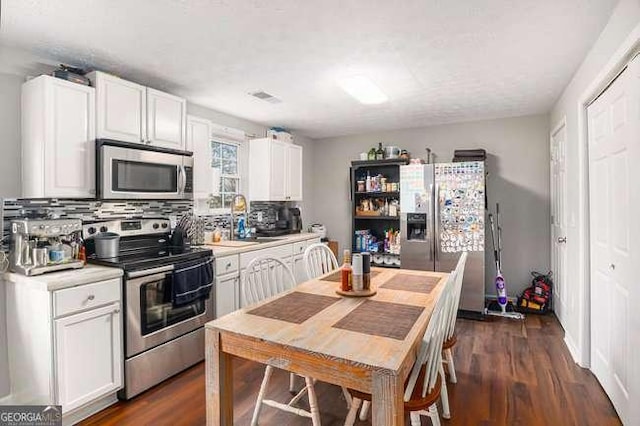 kitchen featuring stainless steel appliances, white cabinets, light countertops, decorative backsplash, and dark wood-style flooring