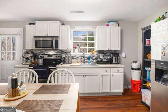 kitchen featuring visible vents, dark wood-type flooring, a sink, backsplash, and stainless steel appliances
