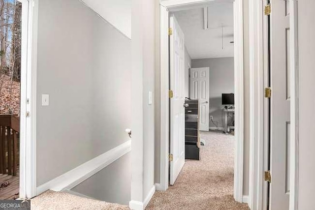 hall with an upstairs landing, baseboards, attic access, and carpet