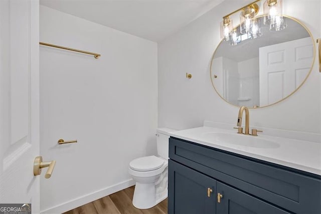 bathroom with vanity, toilet, wood finished floors, and baseboards