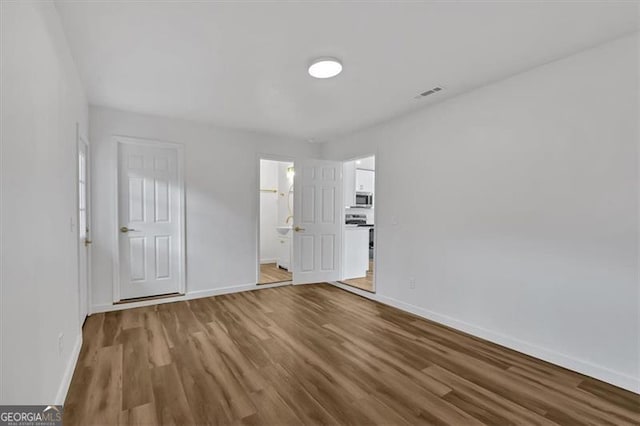 unfurnished bedroom with wood finished floors, visible vents, ensuite bathroom, and baseboards