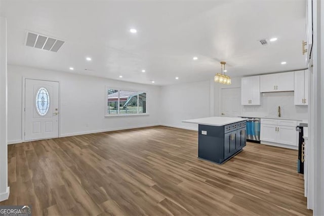 kitchen with visible vents, stainless steel dishwasher, a kitchen island, wood finished floors, and white cabinets