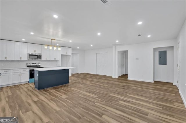 kitchen featuring light wood finished floors, a kitchen island, electric panel, appliances with stainless steel finishes, and white cabinets