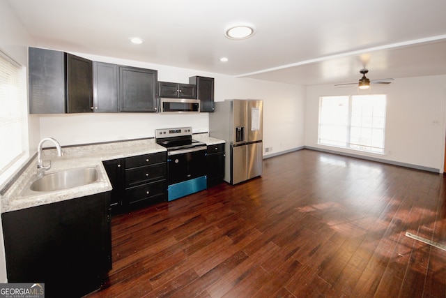 kitchen featuring a sink, dark wood-style floors, stainless steel appliances, light countertops, and dark cabinets