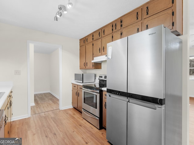 kitchen with baseboards, light countertops, light wood-style floors, under cabinet range hood, and appliances with stainless steel finishes