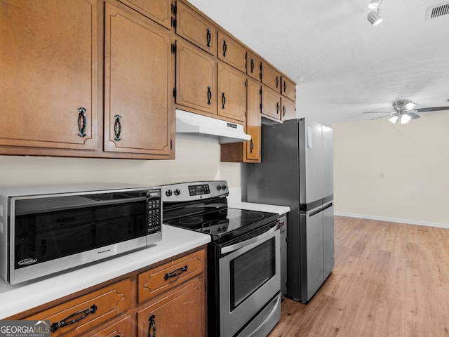 kitchen with light wood finished floors, visible vents, baseboards, under cabinet range hood, and stainless steel appliances