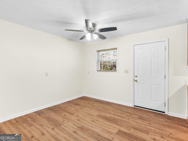 empty room with light wood-type flooring, baseboards, and a textured ceiling