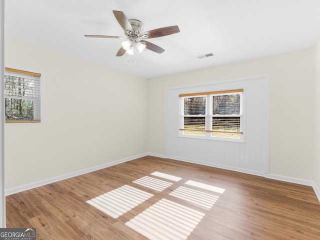 spare room featuring ceiling fan, visible vents, baseboards, and wood finished floors