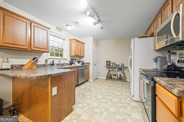 kitchen with a sink, stainless steel appliances, a textured ceiling, dark countertops, and brown cabinets