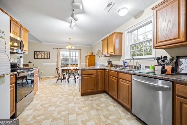 kitchen with visible vents, brown cabinets, dark countertops, stainless steel appliances, and a peninsula