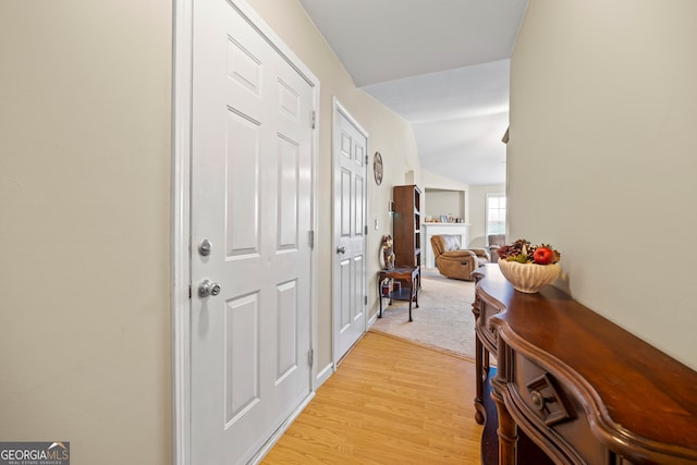 corridor featuring light wood-style flooring and vaulted ceiling