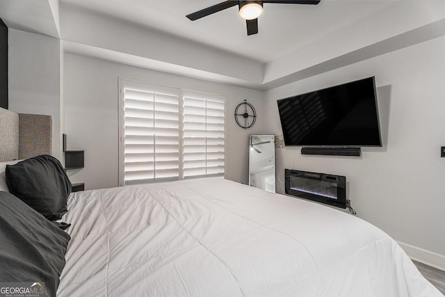 bedroom with a glass covered fireplace, ceiling fan, and wood finished floors