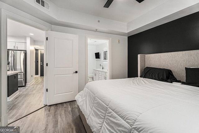 bedroom with visible vents, light wood finished floors, ceiling fan, stainless steel fridge, and connected bathroom