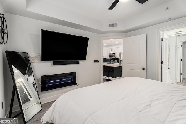 bedroom featuring a tray ceiling, wood finished floors, visible vents, and baseboards