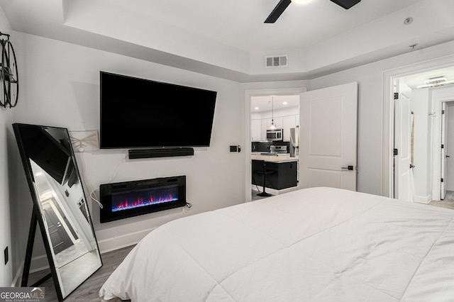 bedroom featuring a tray ceiling, visible vents, baseboards, and wood finished floors