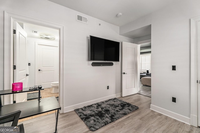 bedroom with visible vents, baseboards, light wood-style floors, and ensuite bath