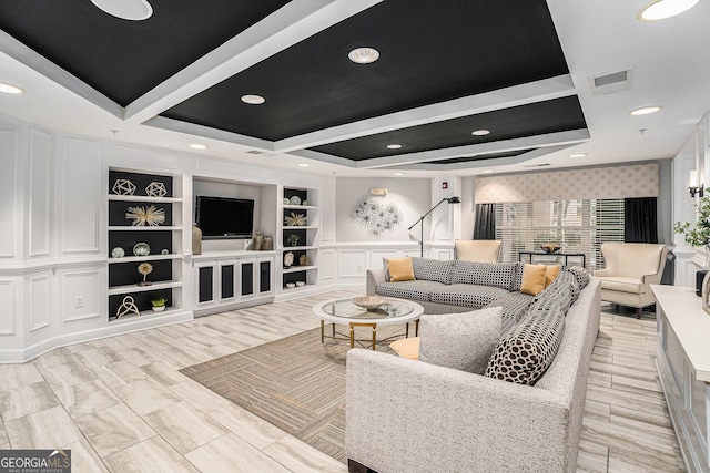 living room with visible vents, built in shelves, recessed lighting, a decorative wall, and a raised ceiling