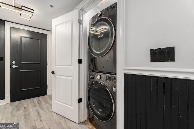 laundry room with laundry area, stacked washer and clothes dryer, light wood-type flooring, and a wainscoted wall