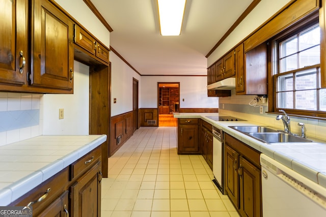 kitchen featuring tile counters, under cabinet range hood, wainscoting, black electric cooktop, and a sink