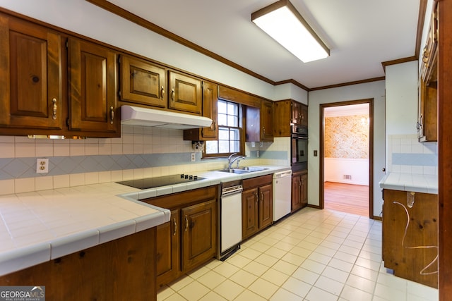 kitchen featuring tile countertops, a sink, black appliances, under cabinet range hood, and crown molding