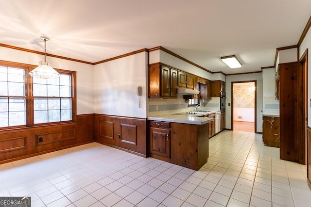 kitchen with a wainscoted wall, under cabinet range hood, crown molding, light tile patterned floors, and tile counters