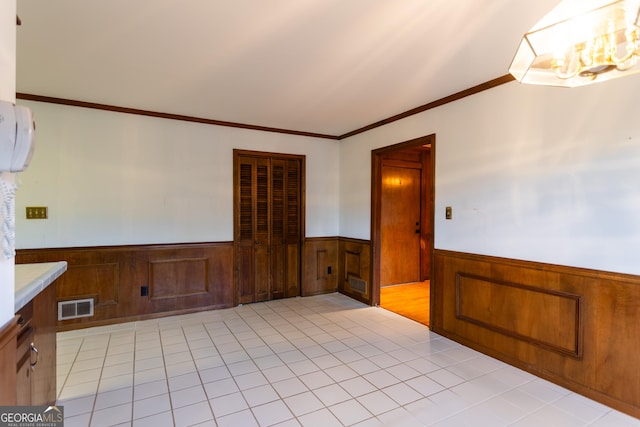 spare room featuring visible vents, a wainscoted wall, wood walls, crown molding, and light tile patterned floors