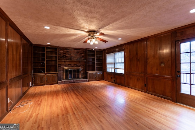 unfurnished living room featuring a brick fireplace, light wood-style floors, wood walls, and a textured ceiling