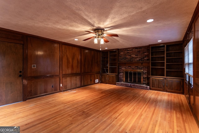 unfurnished living room with light wood-style flooring, built in shelves, a textured ceiling, and a brick fireplace