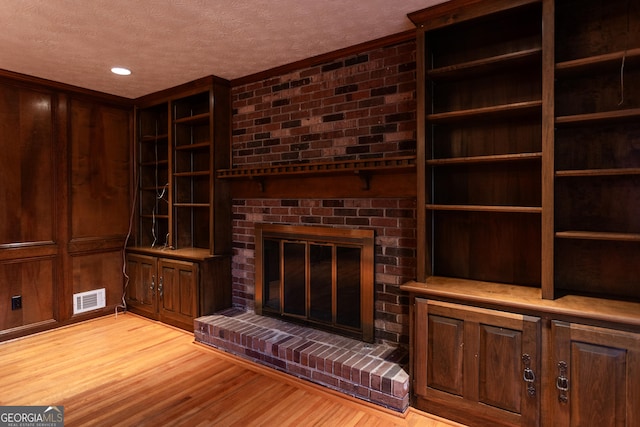 unfurnished living room featuring visible vents, a textured ceiling, wood finished floors, wood walls, and a fireplace