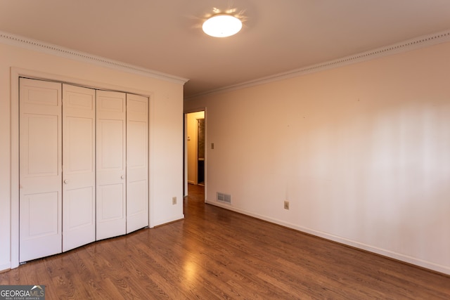 unfurnished bedroom with visible vents, ornamental molding, wood finished floors, a closet, and baseboards