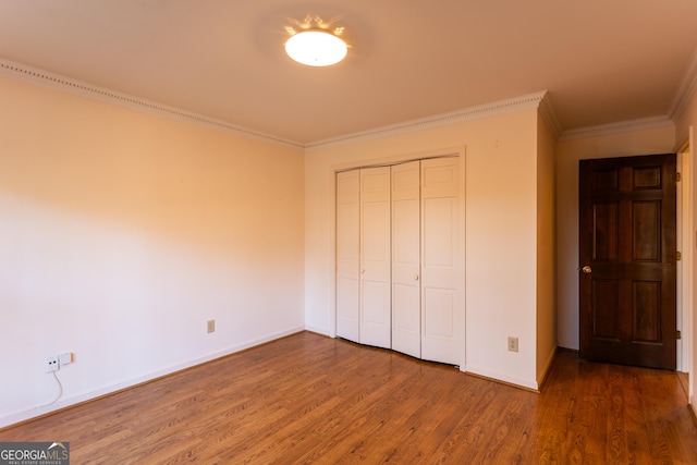 unfurnished bedroom with crown molding, wood finished floors, a closet, and baseboards