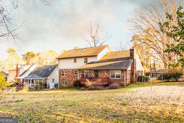 rear view of property featuring a deck, a chimney, a yard, and fence