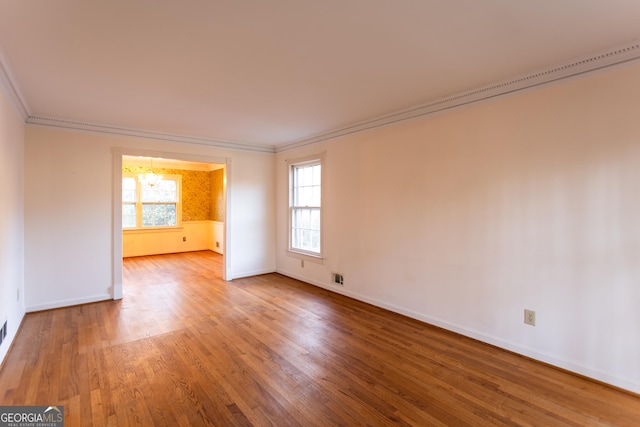 spare room featuring visible vents, a notable chandelier, ornamental molding, wood finished floors, and baseboards