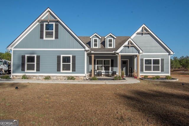 craftsman inspired home featuring board and batten siding, covered porch, a front lawn, and roof with shingles