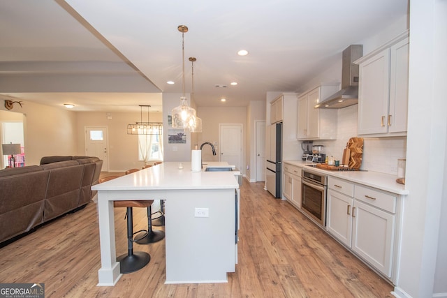 kitchen featuring open floor plan, a kitchen bar, light wood-style flooring, appliances with stainless steel finishes, and wall chimney exhaust hood