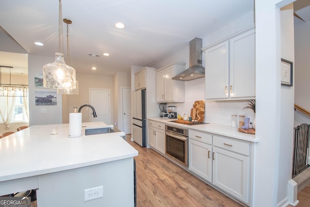 kitchen with backsplash, light countertops, stainless steel oven, light wood-style flooring, and wall chimney exhaust hood