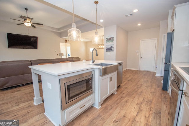 kitchen with a sink, open floor plan, appliances with stainless steel finishes, white cabinets, and light wood finished floors