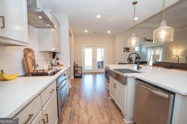 kitchen featuring wall chimney range hood, decorative backsplash, french doors, stainless steel appliances, and a sink