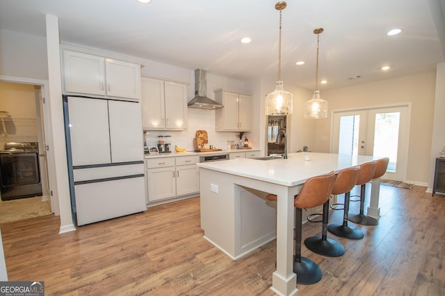 kitchen featuring washer / clothes dryer, freestanding refrigerator, a sink, french doors, and wall chimney range hood