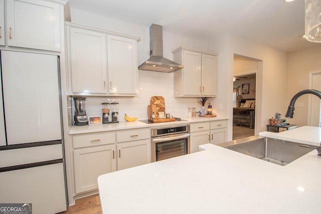 kitchen featuring oven, a sink, freestanding refrigerator, stovetop, and wall chimney range hood