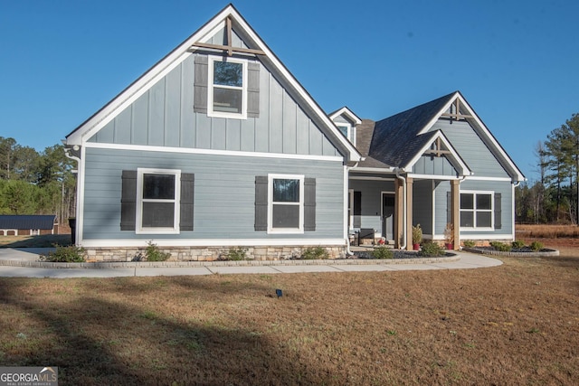 view of front of property featuring board and batten siding, covered porch, a front yard, and a shingled roof