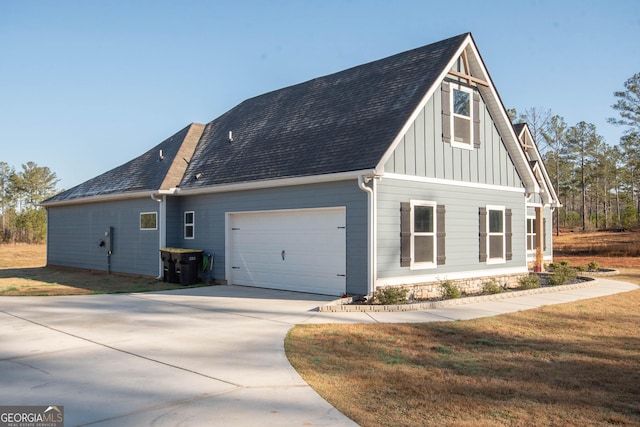 view of side of home with board and batten siding, a shingled roof, driveway, and a yard