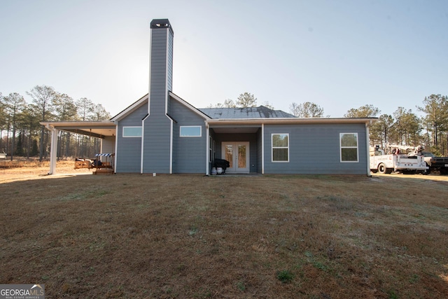 rear view of house featuring a carport, french doors, a yard, and a chimney