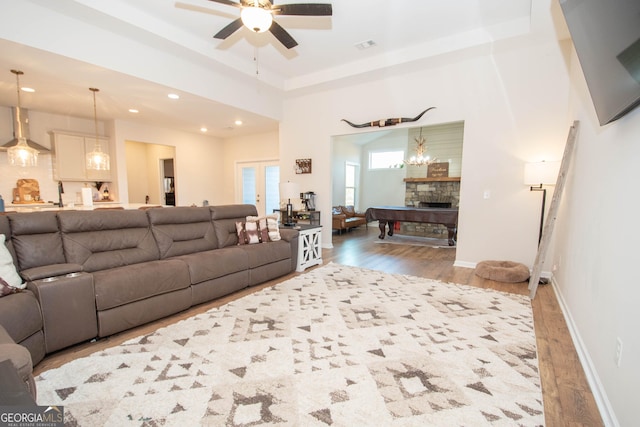 living area featuring a stone fireplace, a raised ceiling, wood finished floors, and baseboards