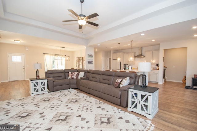 living room featuring baseboards, a tray ceiling, ceiling fan with notable chandelier, recessed lighting, and light wood-style floors