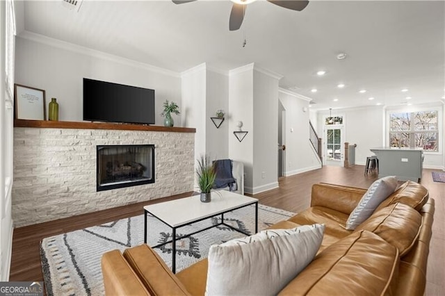 living room with wood finished floors, crown molding, a fireplace, and ceiling fan